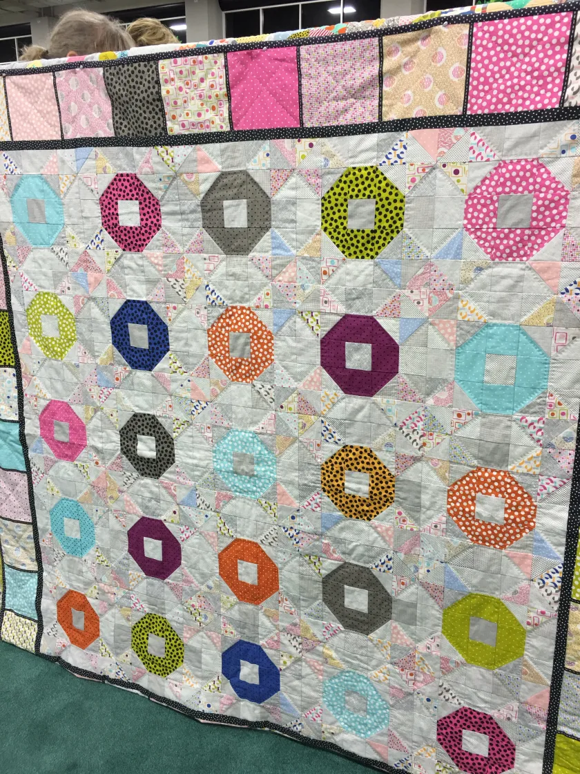 Patchwork quilt with colorful circular medallion patterns in pink, gold, teal, and purple against gray background