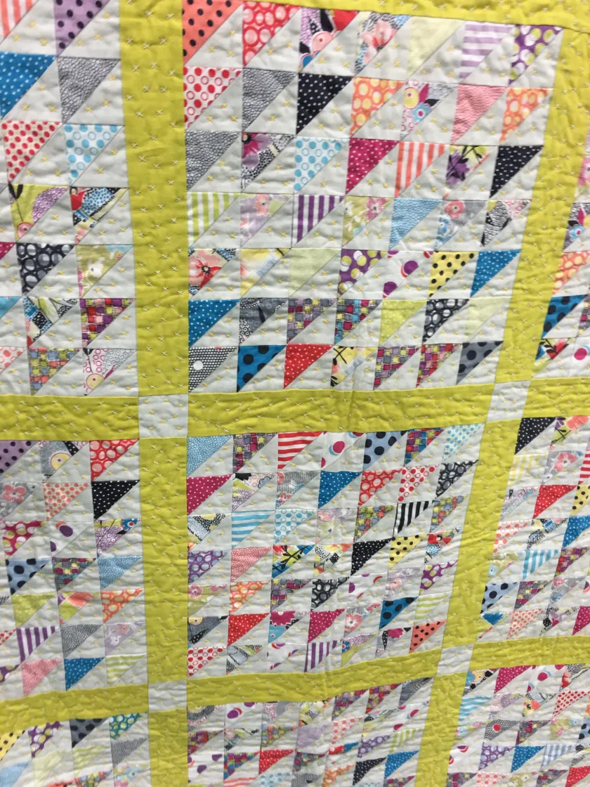 Quilt made of colorful triangle patchwork squares separated by yellow-green sashing strips, bright crisp daylight mood