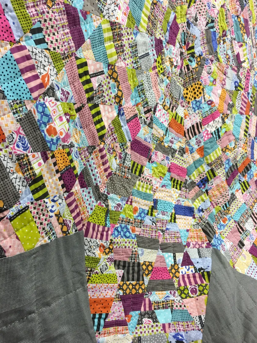 Colorful patchwork quilt with many small multicolored printed fabric pieces and a dark grid pattern