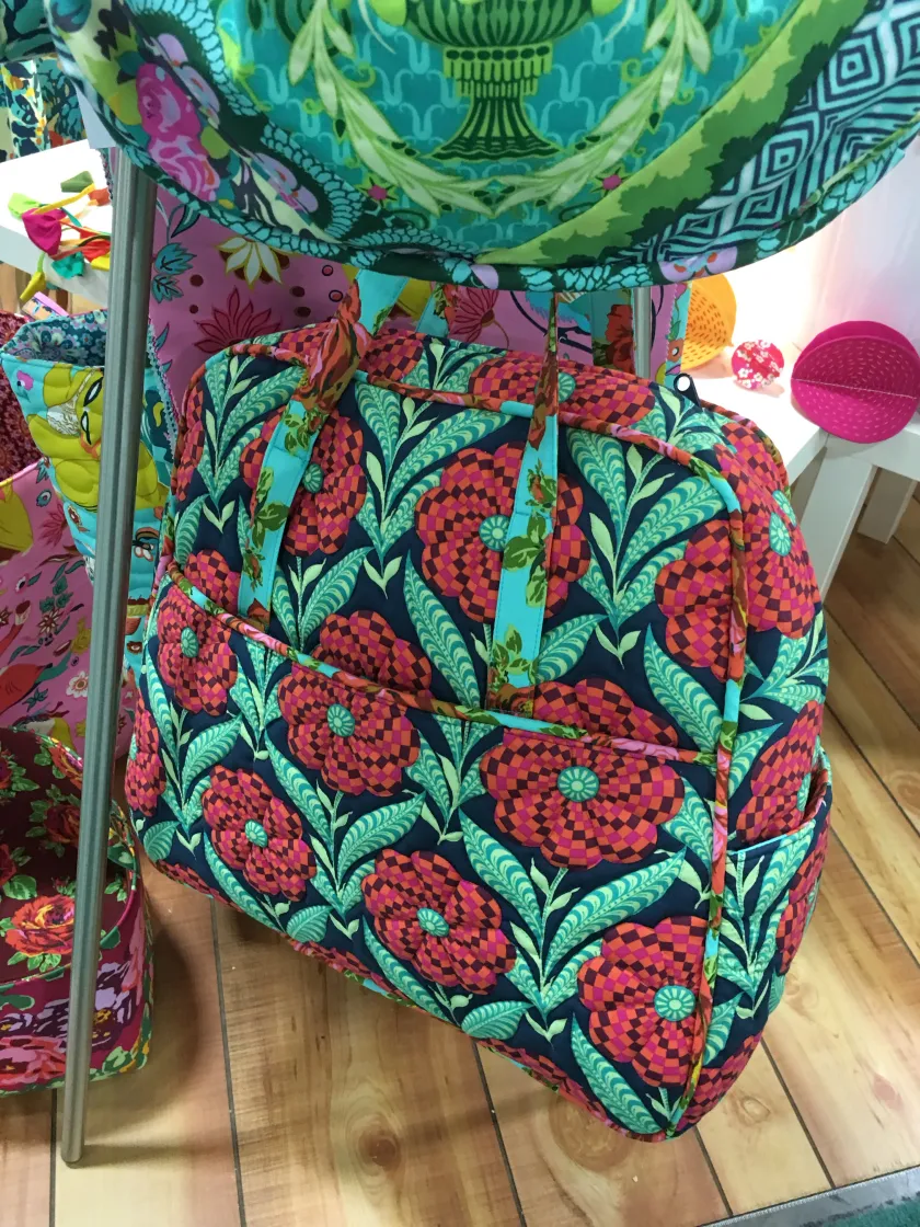 Quilted bag with bold floral and geometric print in red, pink, teal and navy, displayed on a rack indoors with wood flooring