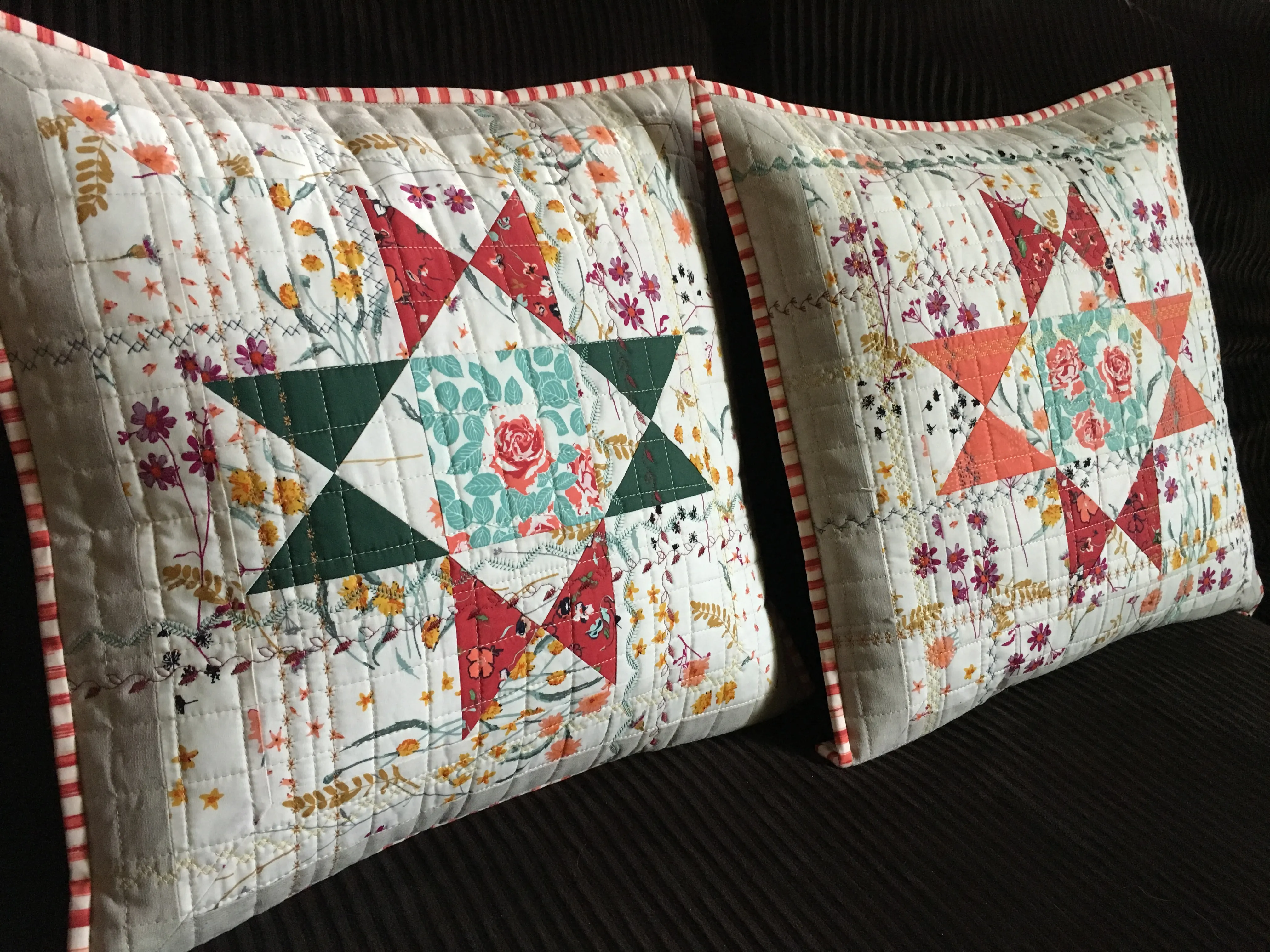 Two floral patchwork quilted pillows with star patterns in red, green, teal and orange on a dark sofa, cozy handmade mood