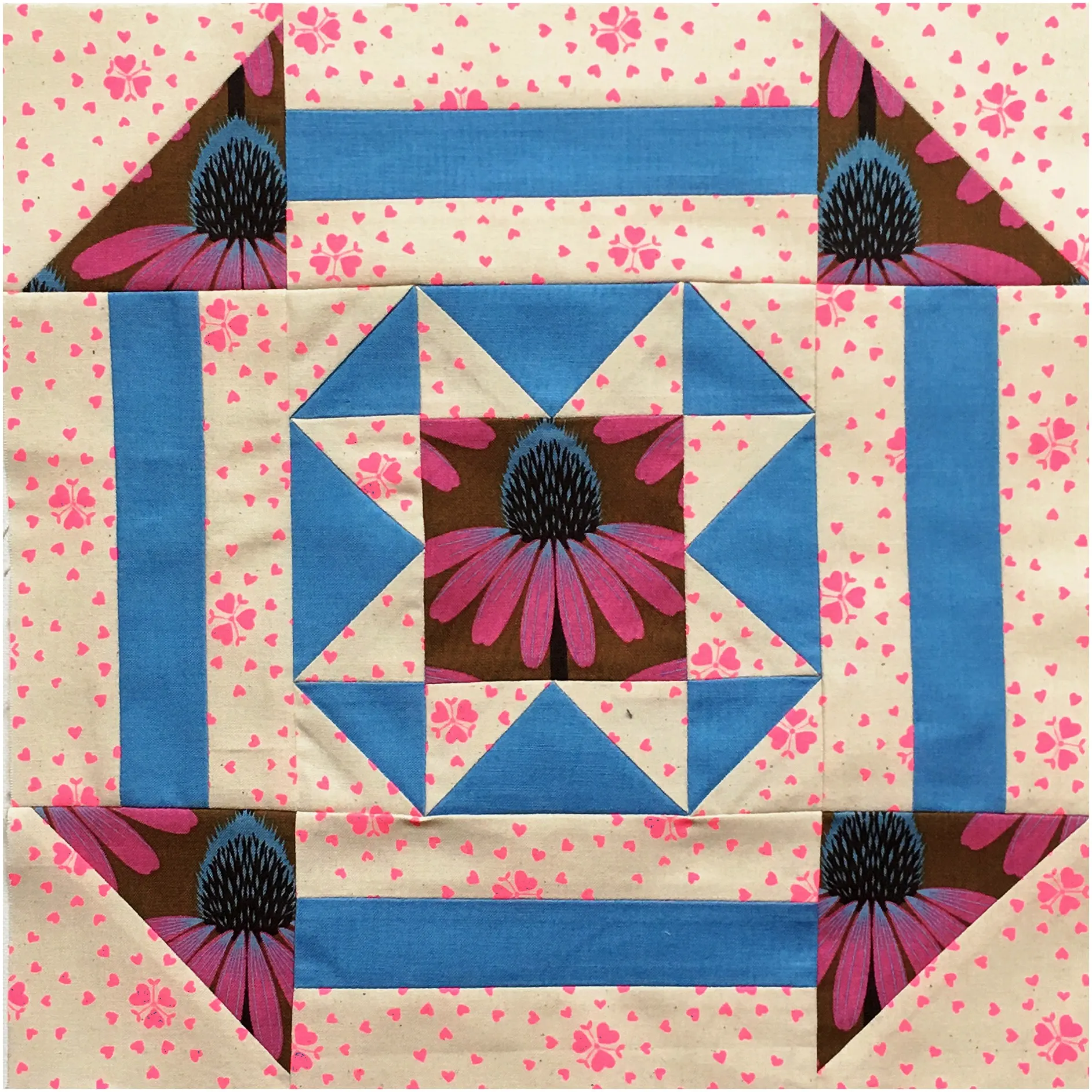 Quilt block with a central pink and brown floral medallion, blue star pattern, and cream fabric with pink heart print border, bright cheerful mood